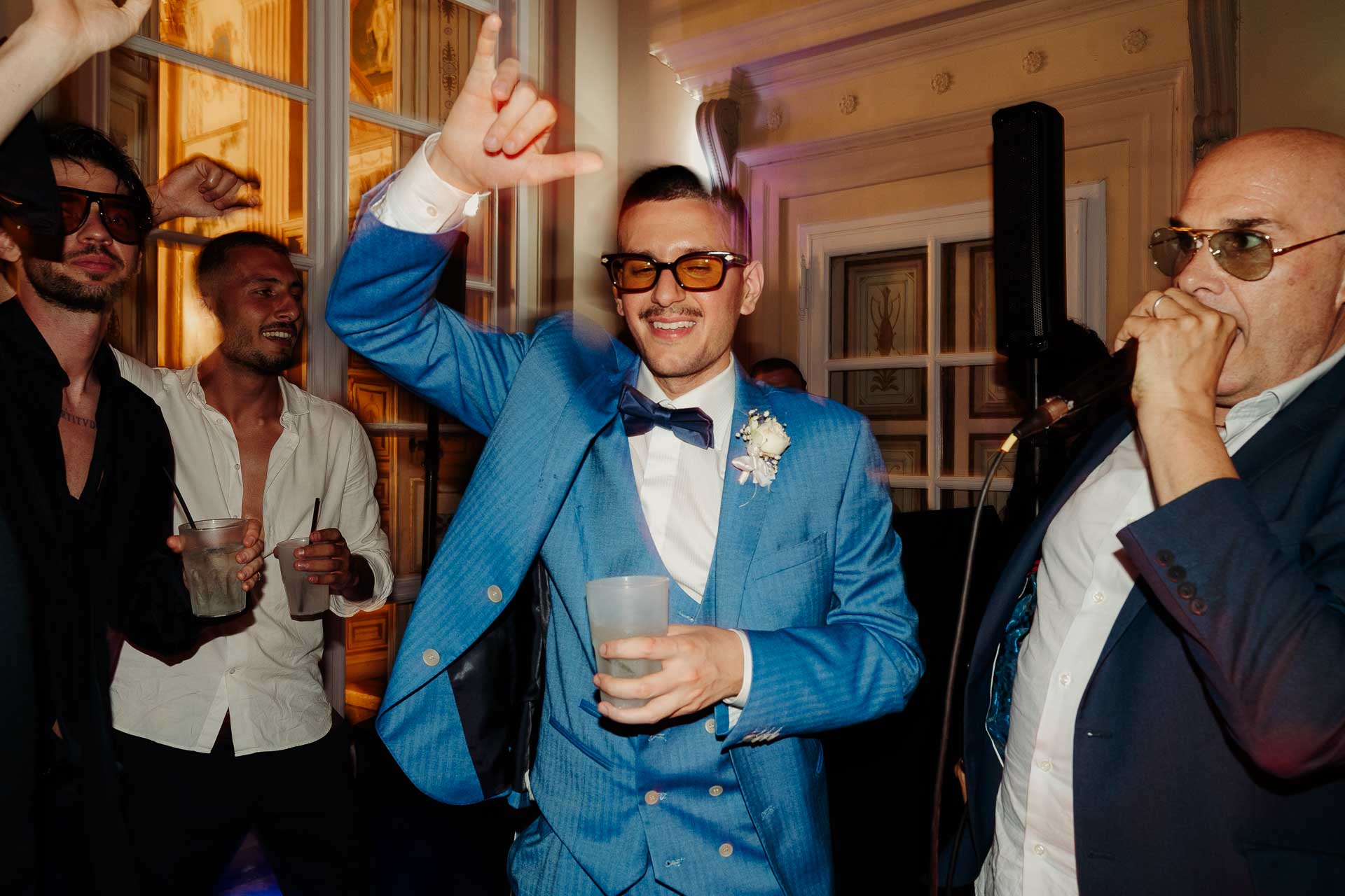 Un amico in completo azzurro balla con un bicchiere in mano, tra gli invitati