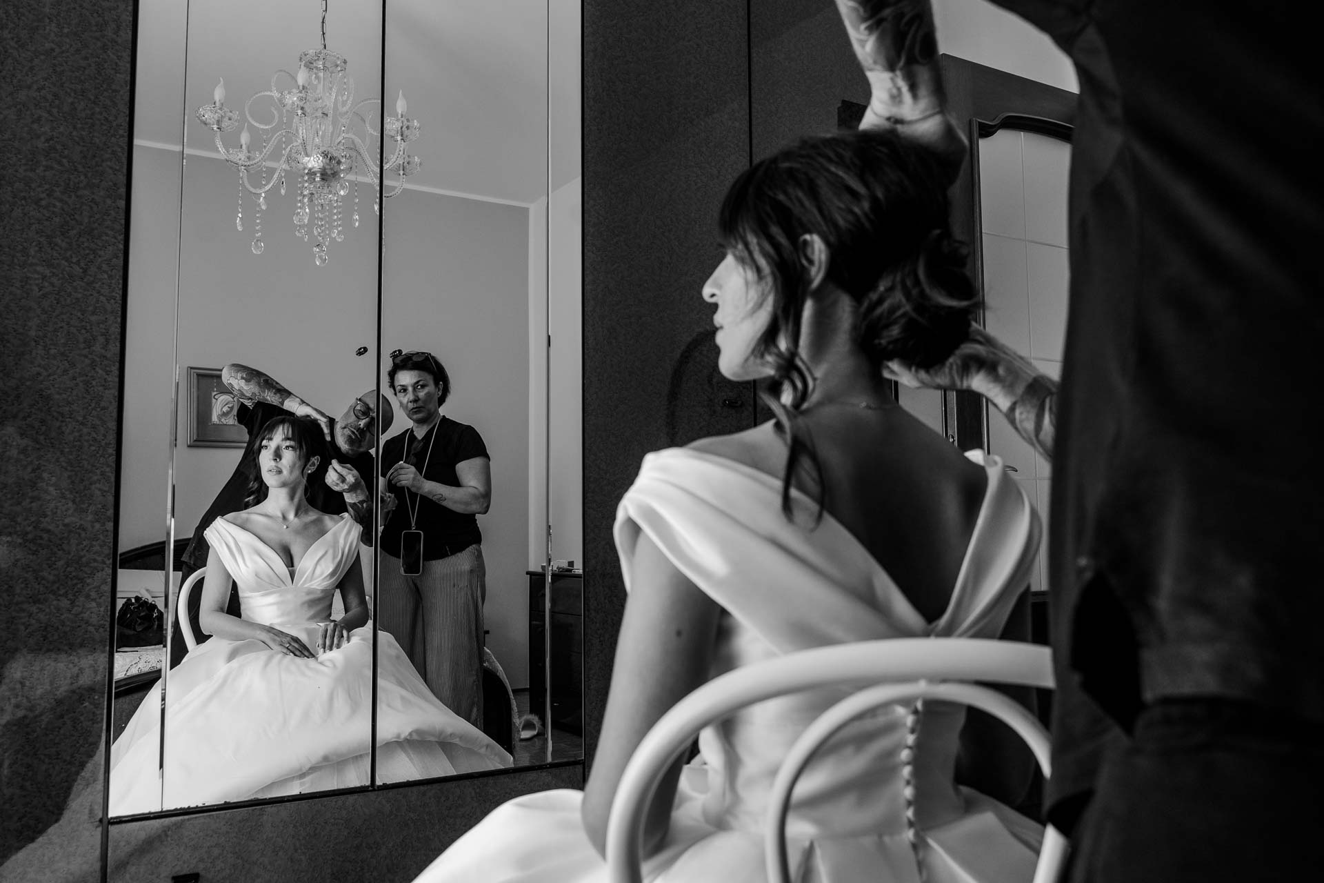 In bianco e nero, il parrucchiere sistema l'acconciatura della sposa, riflessa nello specchio