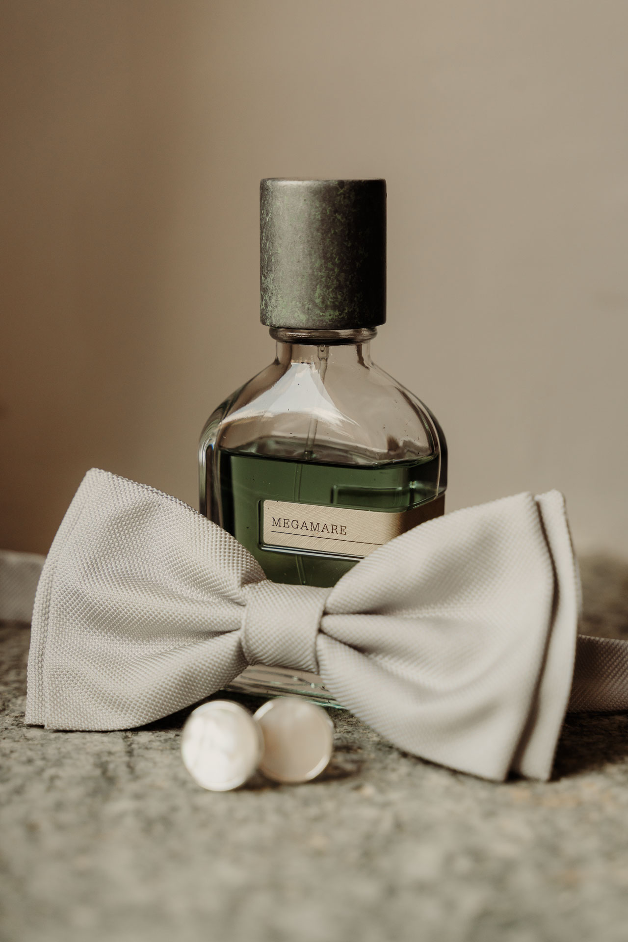 Il papillon grigio perla, i gemelli di madreperla e il flacone di profumo sul tappeto