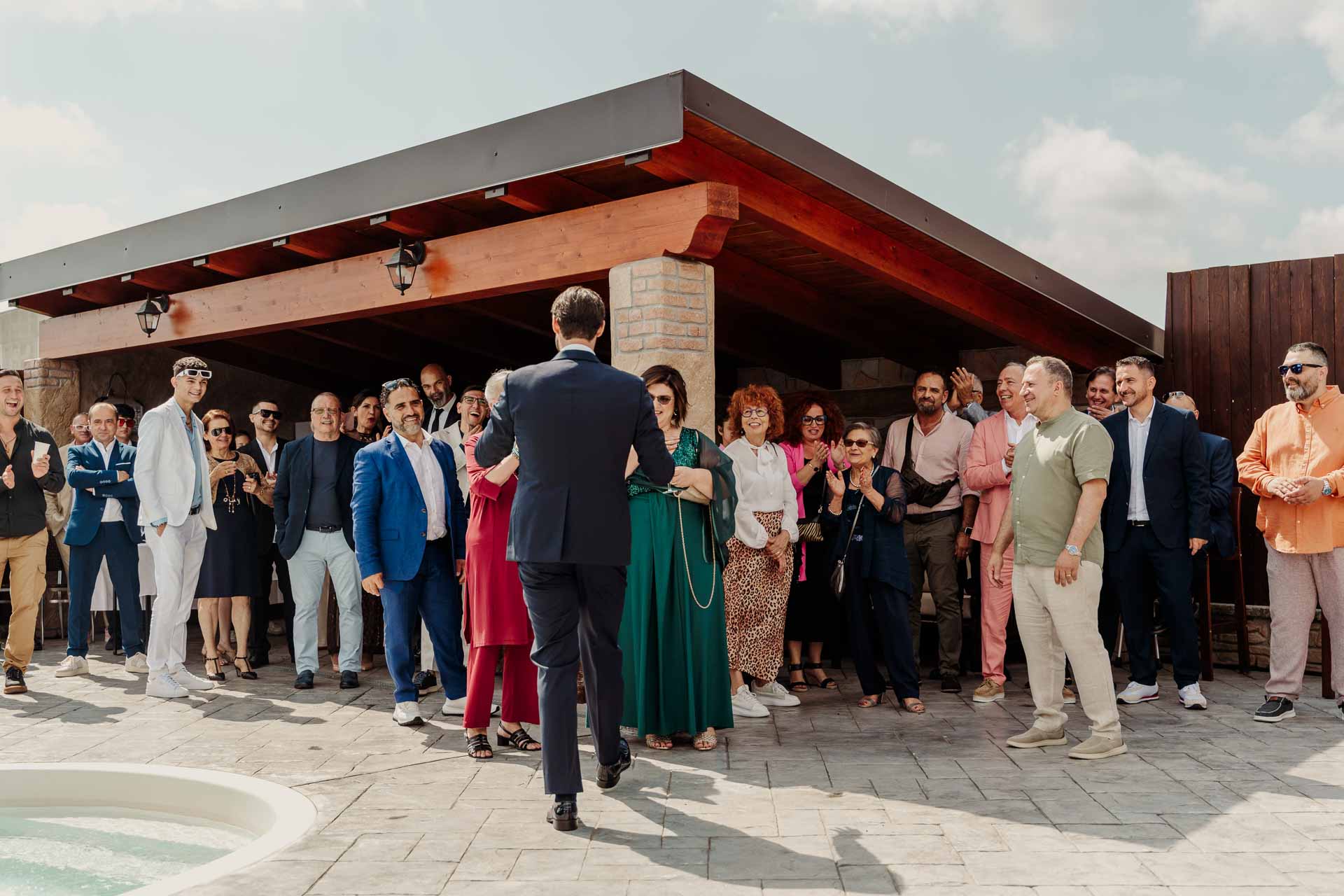 Lo sposo di spalle cammina verso gli invitati radunati sotto il portico