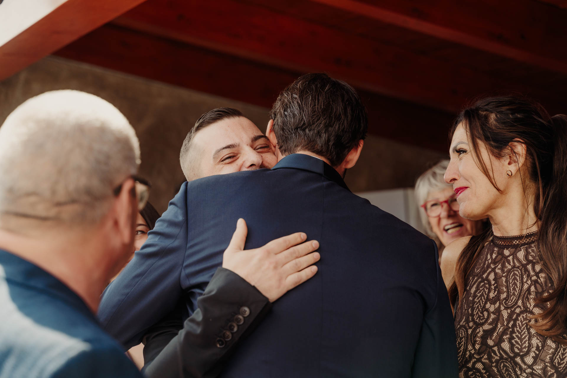 Lo sposo abbraccia un amico, tra gli invitati sotto il portico