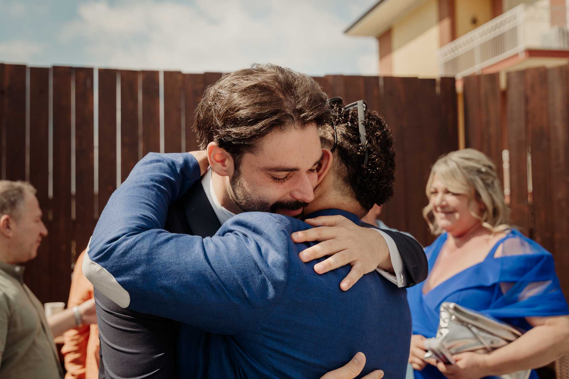 Lo sposo stringe in un abbraccio un amico, accanto a una signora in blu che ride