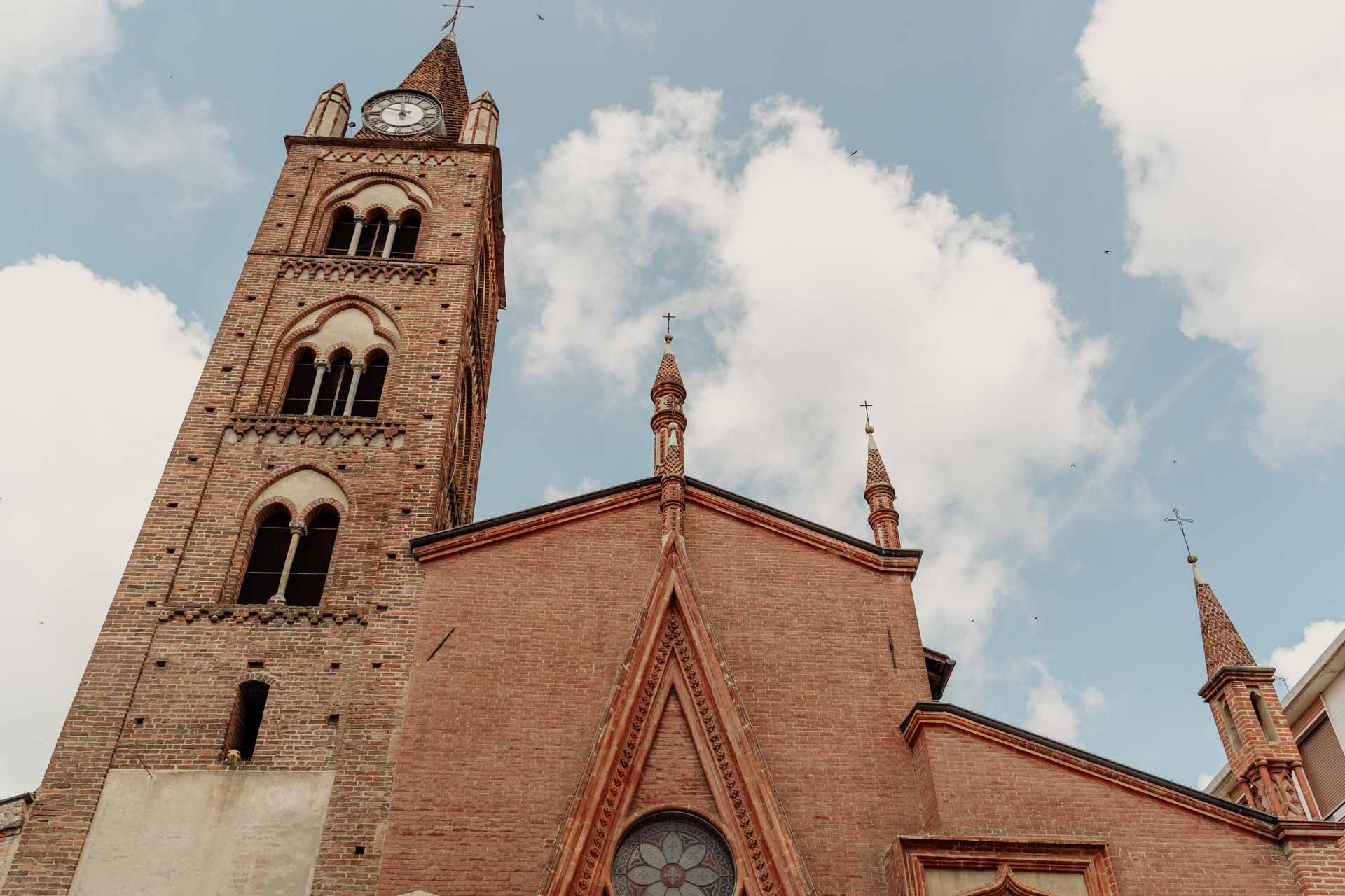 Il campanile di mattoni rossi e la facciata del Duomo di San Giovanni Battista a Ciriè, sotto un cielo di nuvole