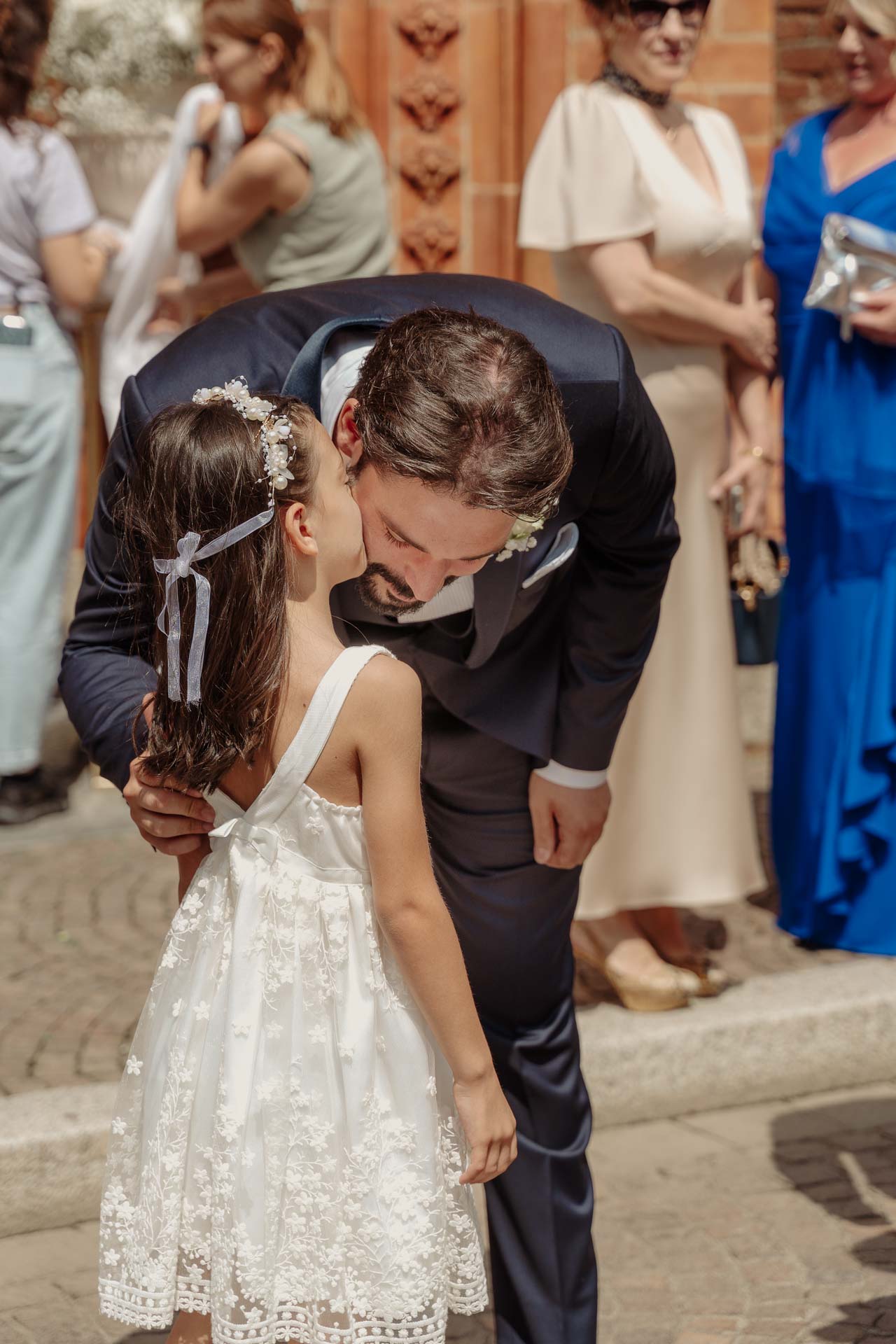 Lo sposo si china a baciare sulla guancia una bambina con l'abito di pizzo