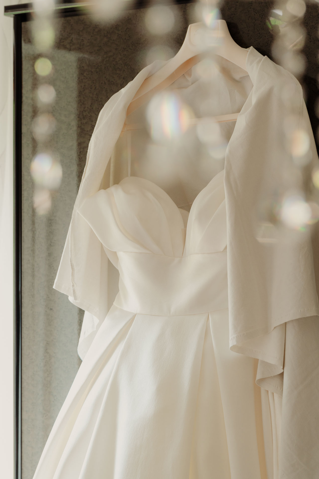 L'abito da sposa appeso davanti allo specchio, tra i cristalli del lampadario
