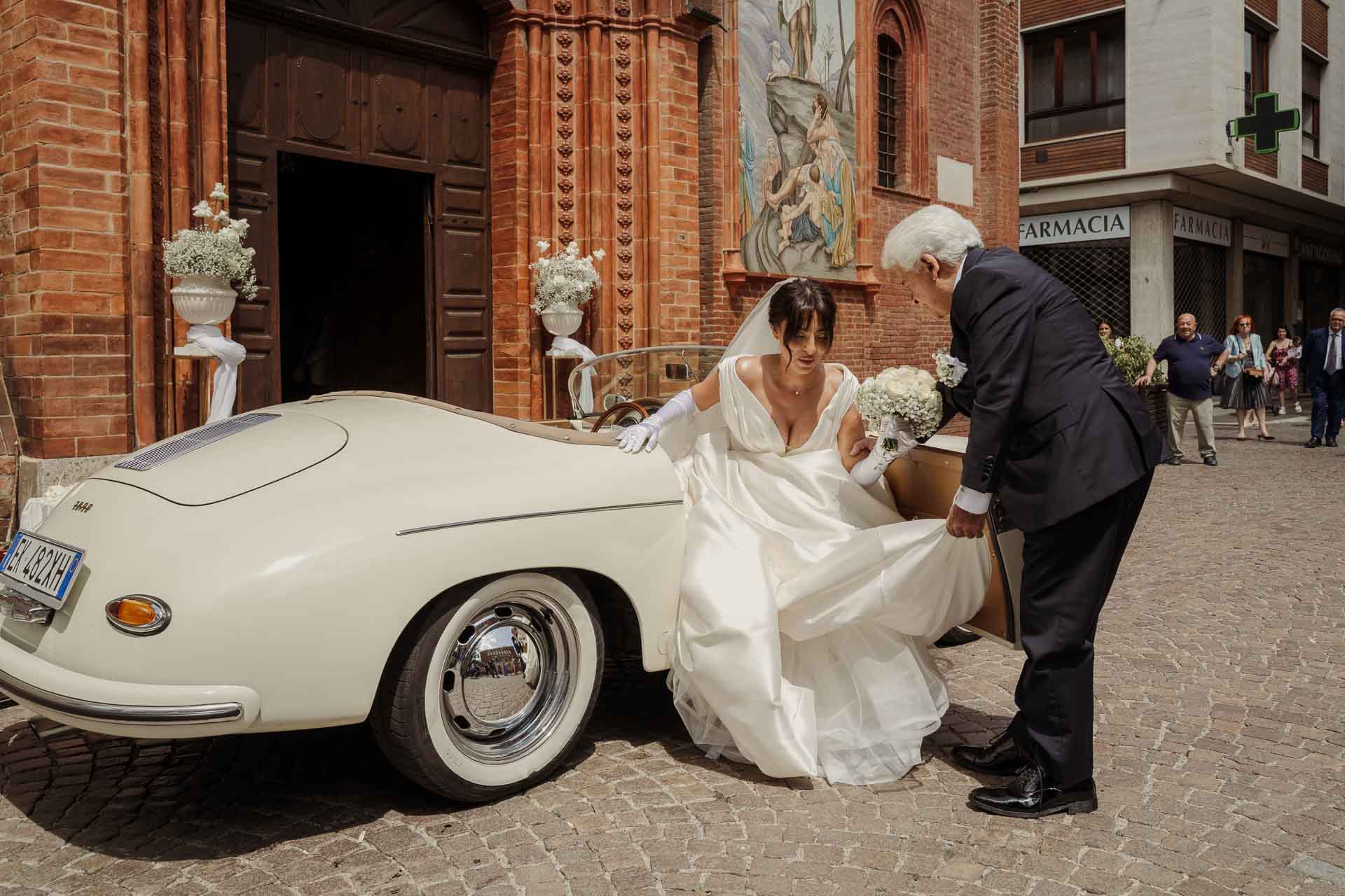 La sposa scende dall'auto d'epoca davanti al portone della chiesa, aiutata da un signore in abito scuro