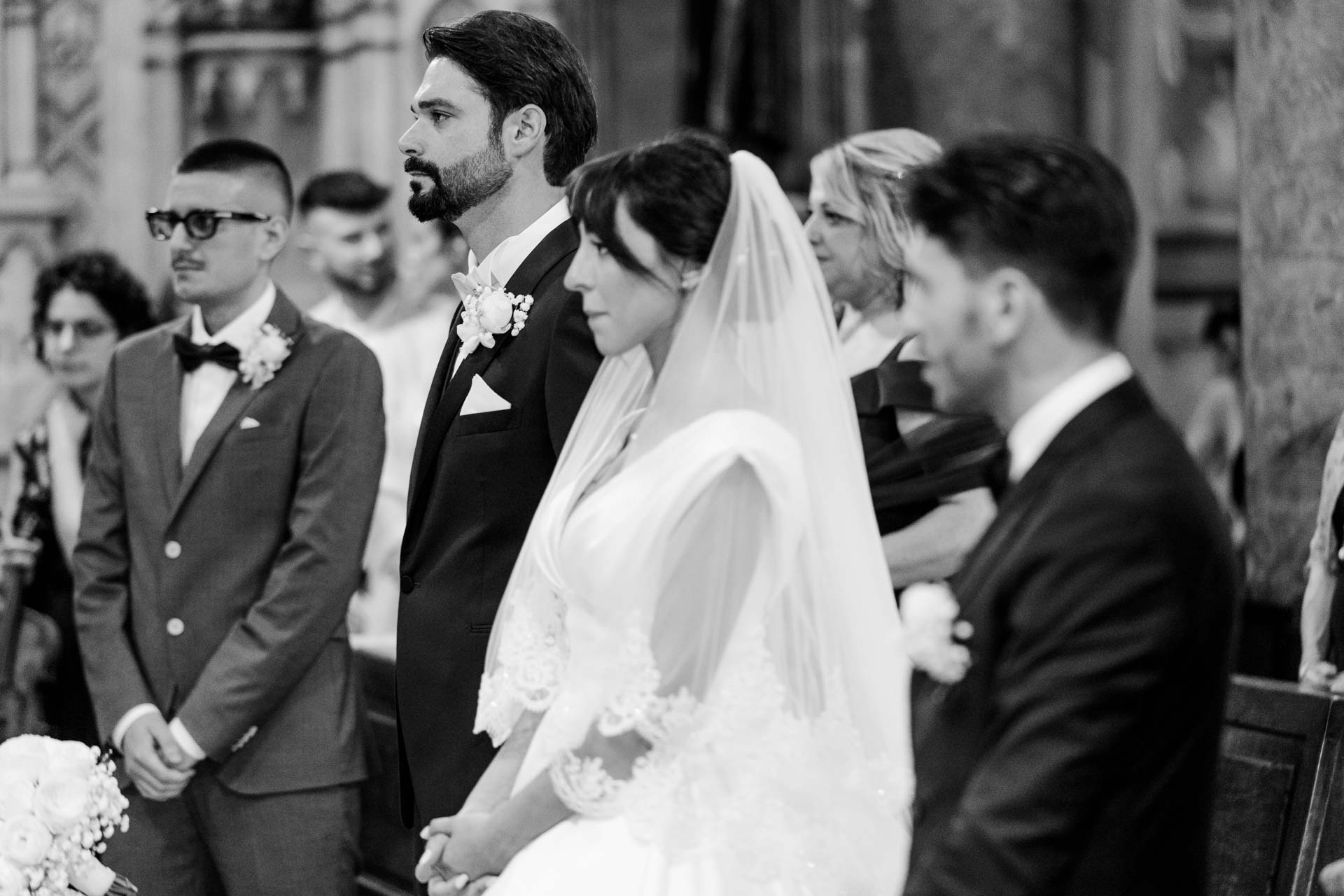 In bianco e nero, gli sposi in piedi in prima fila, circondati dagli invitati