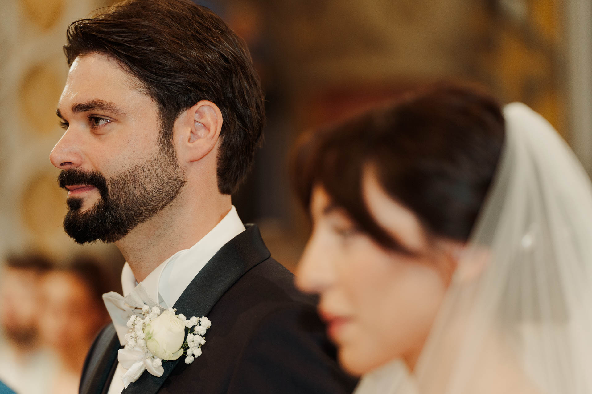 Lo sposo di profilo, con la sposa velata sfocata in primo piano