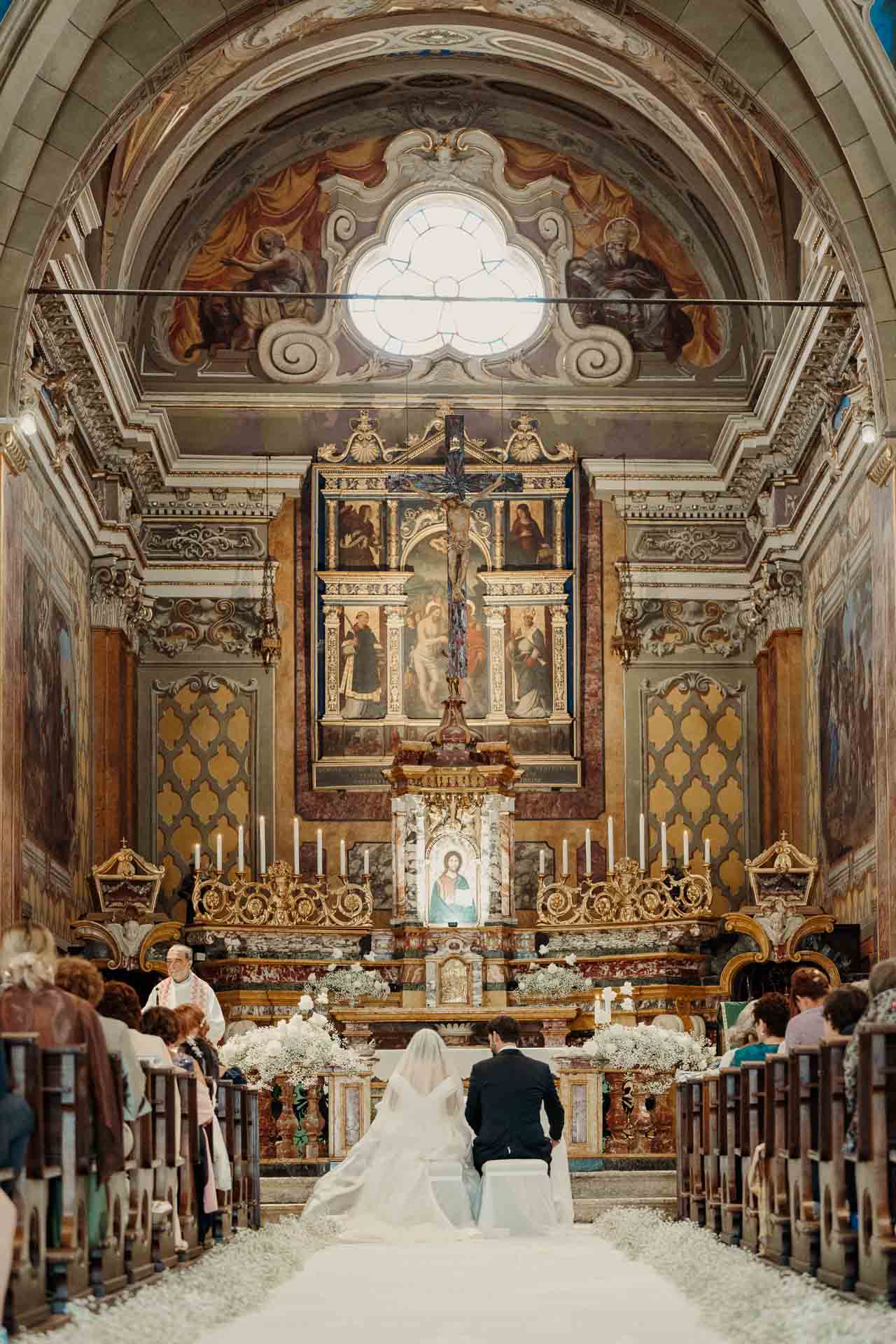 Gli sposi di spalle, inginocchiati davanti all'altare, visti dal fondo della navata