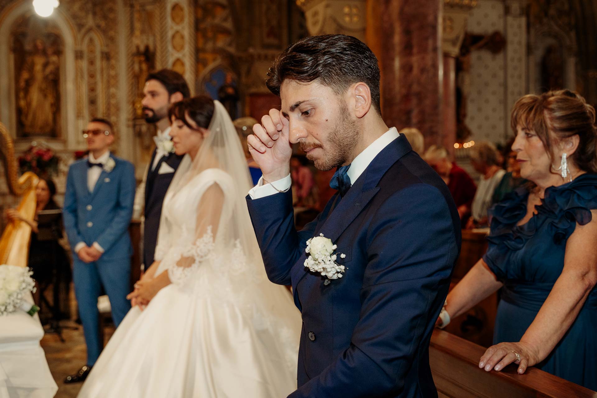 Un amico in giacca blu si asciuga una lacrima accanto agli sposi