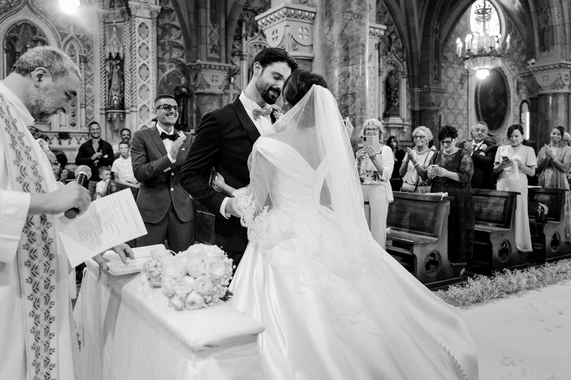 In bianco e nero, il bacio degli sposi davanti all'altare, con il sacerdote accanto