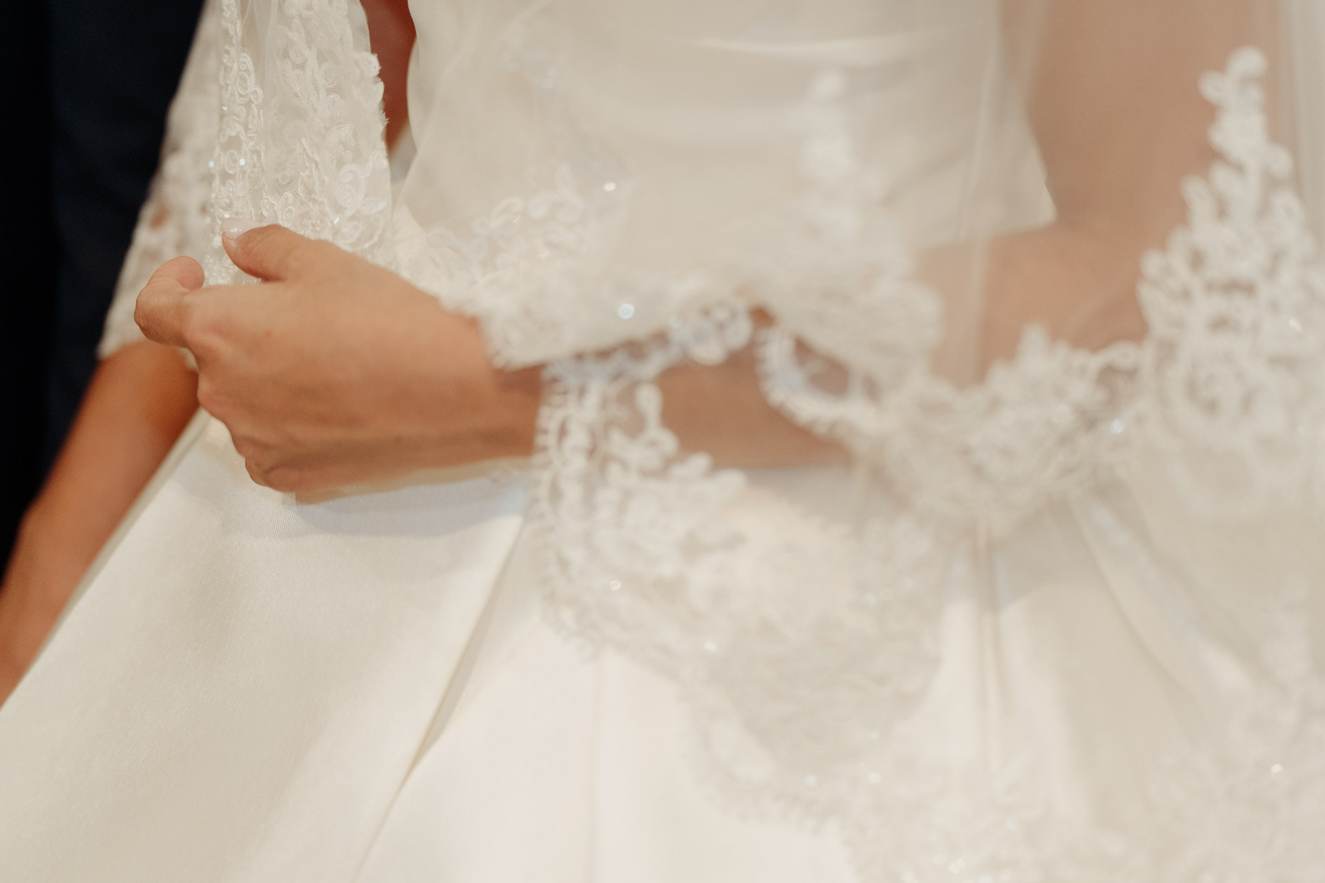 Le mani della sposa sul pizzo ricamato della manica