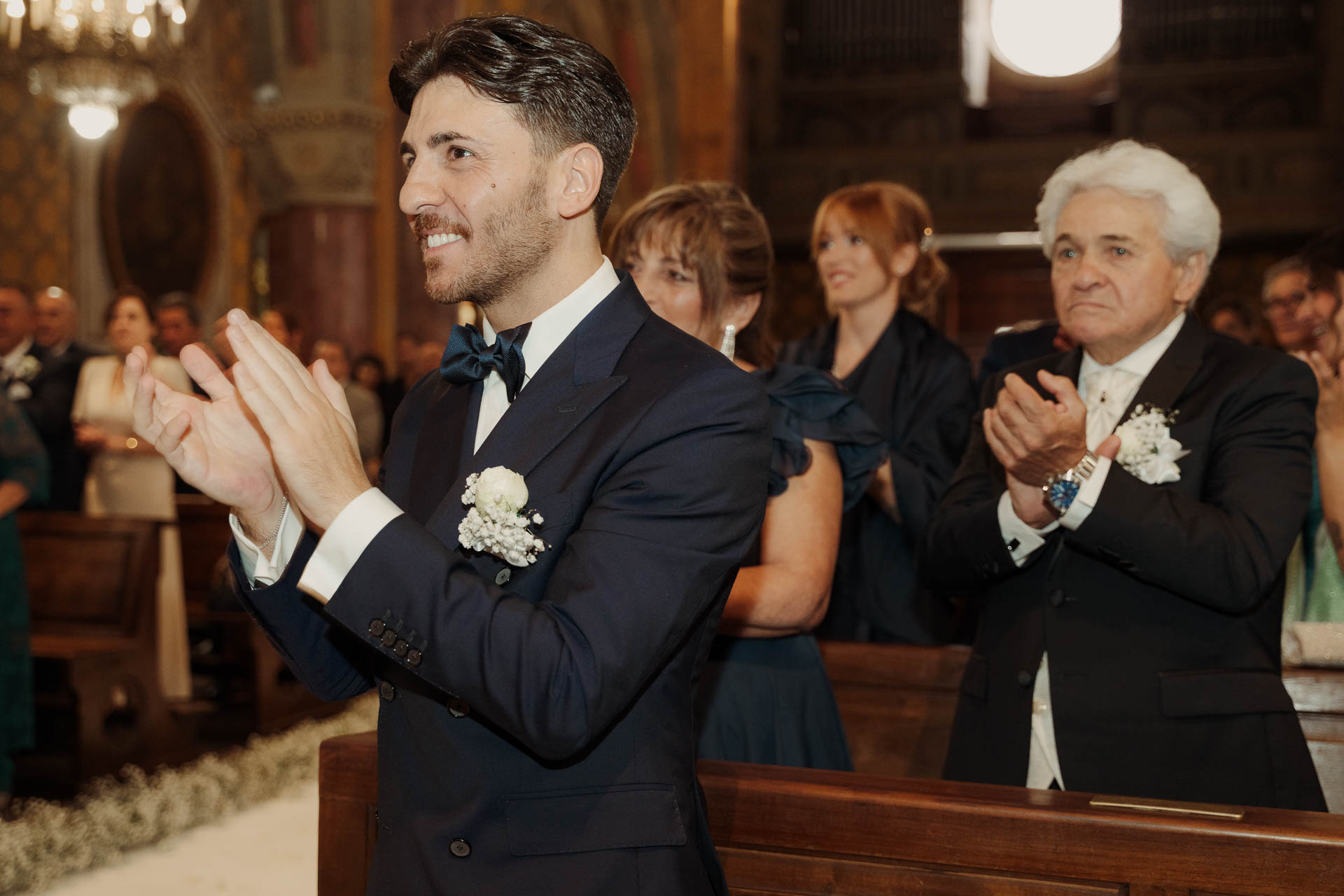 Lo sposo e un signore dai capelli bianchi applaudono sorridendo nel banco