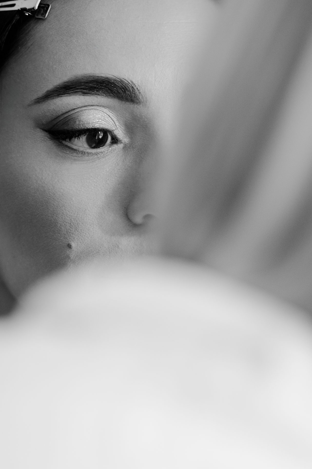 In bianco e nero, l'occhio della sposa con il trucco appena fatto, dietro il bordo della vestaglia