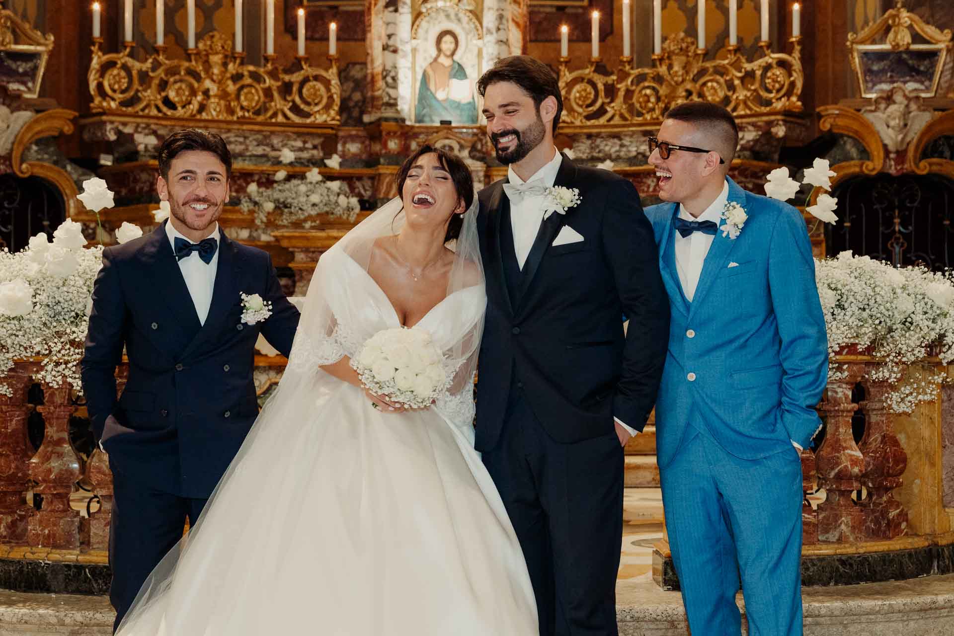 Gli sposi e due amici in posa davanti all'altare dorato, tra le risate
