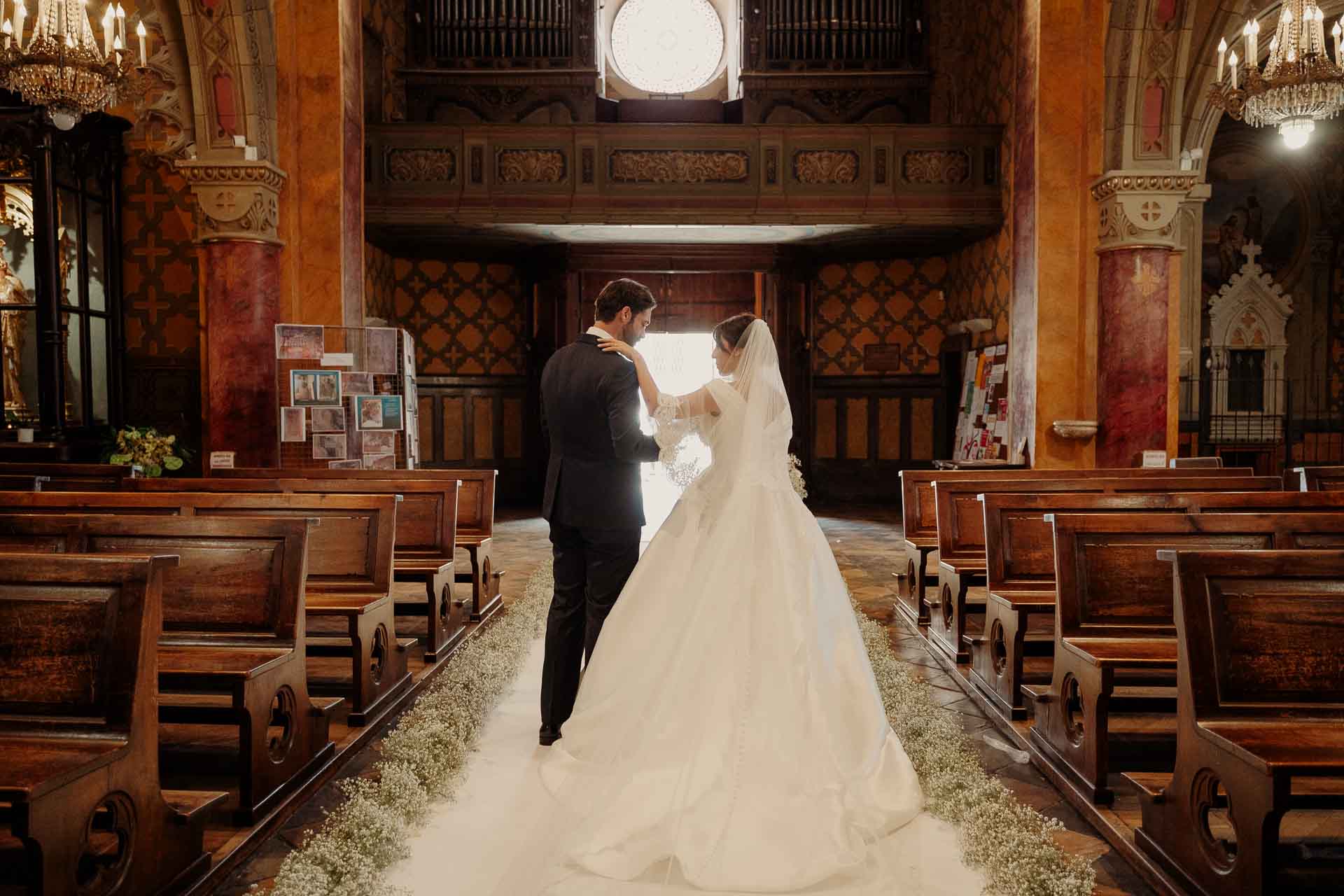 Gli sposi di spalle percorrono la navata sul tappeto di gypsophila, verso la luce del portone