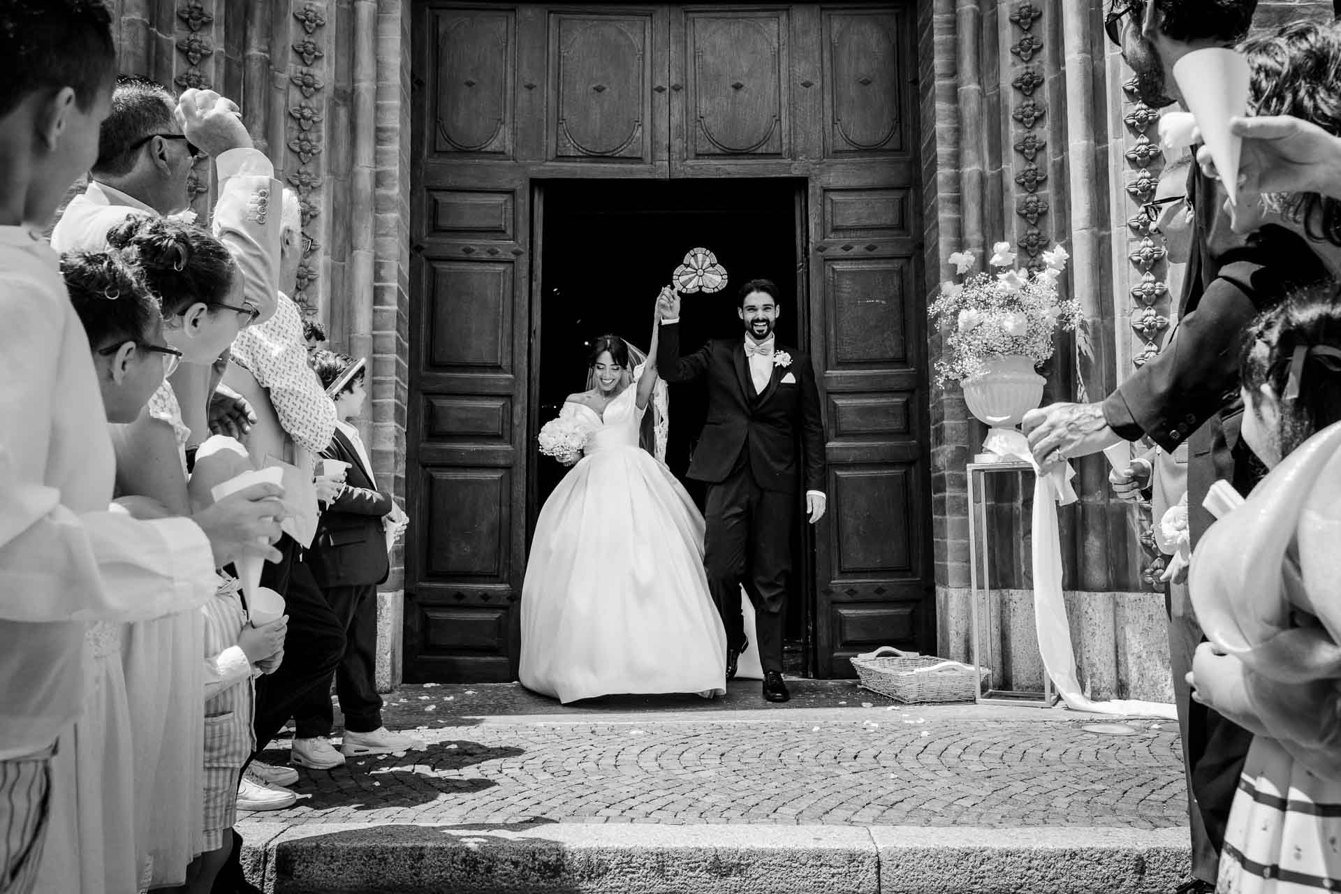 In bianco e nero, gli sposi escono dal portone della chiesa, tra gli invitati