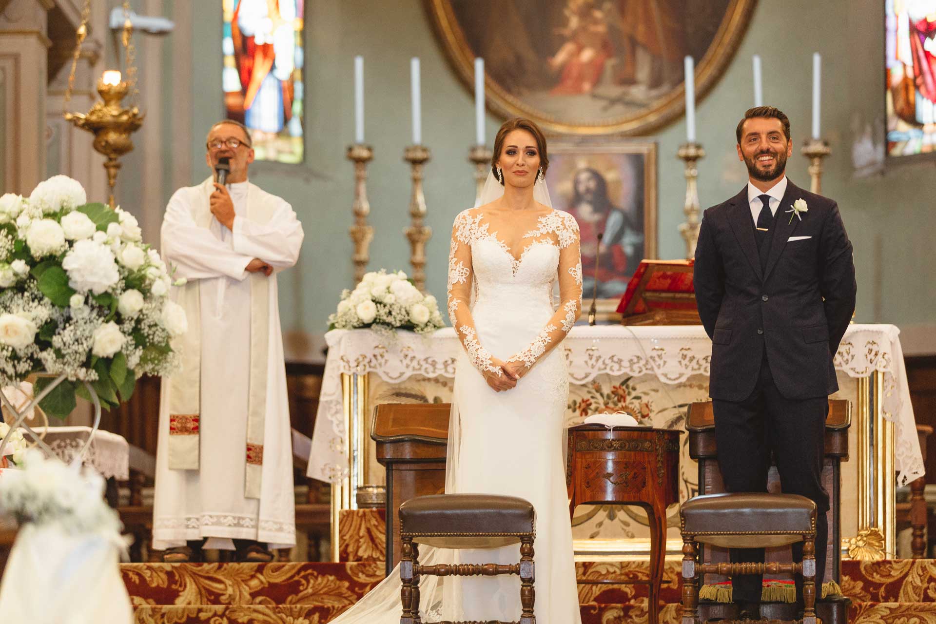 Il sacerdote parla al microfono, gli sposi in piedi all'altare