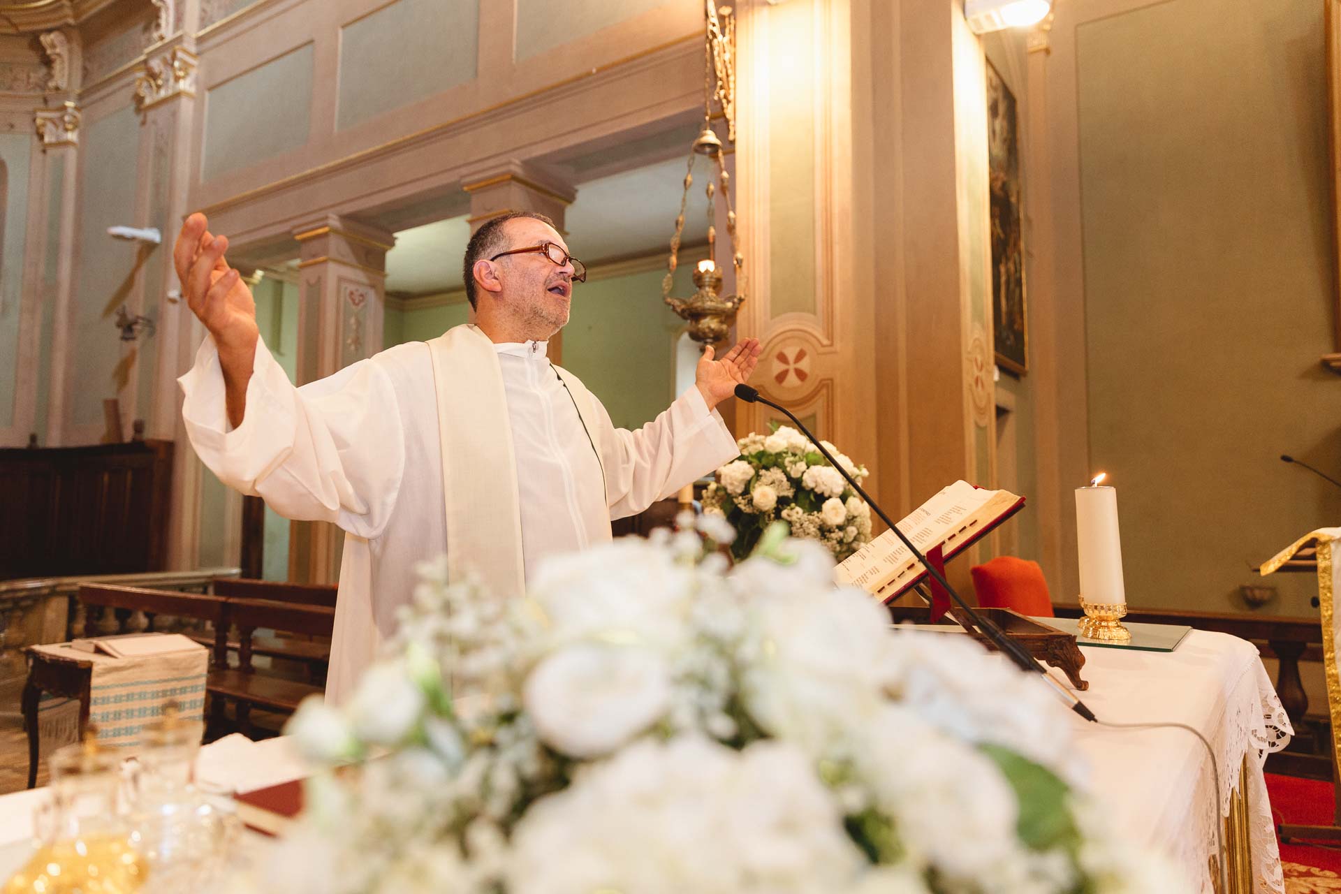 Il sacerdote benedice gli sposi, tra i fiori bianchi