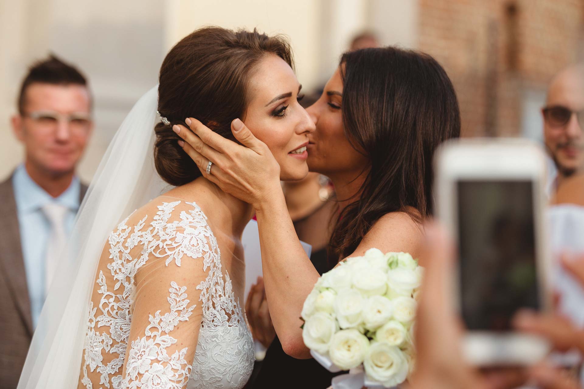 Un'amica bacia la sposa sulla guancia, tra i telefoni degli invitati