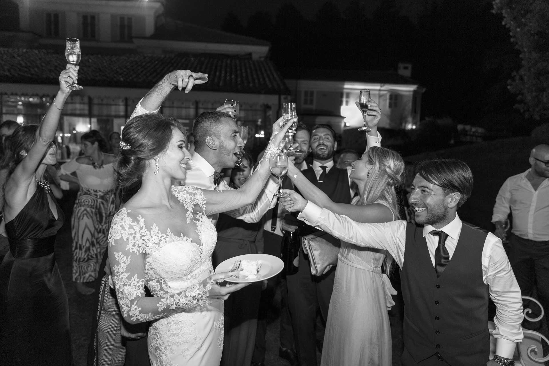 In bianco e nero, la sposa con il piatto della torta tra gli amici che brindano