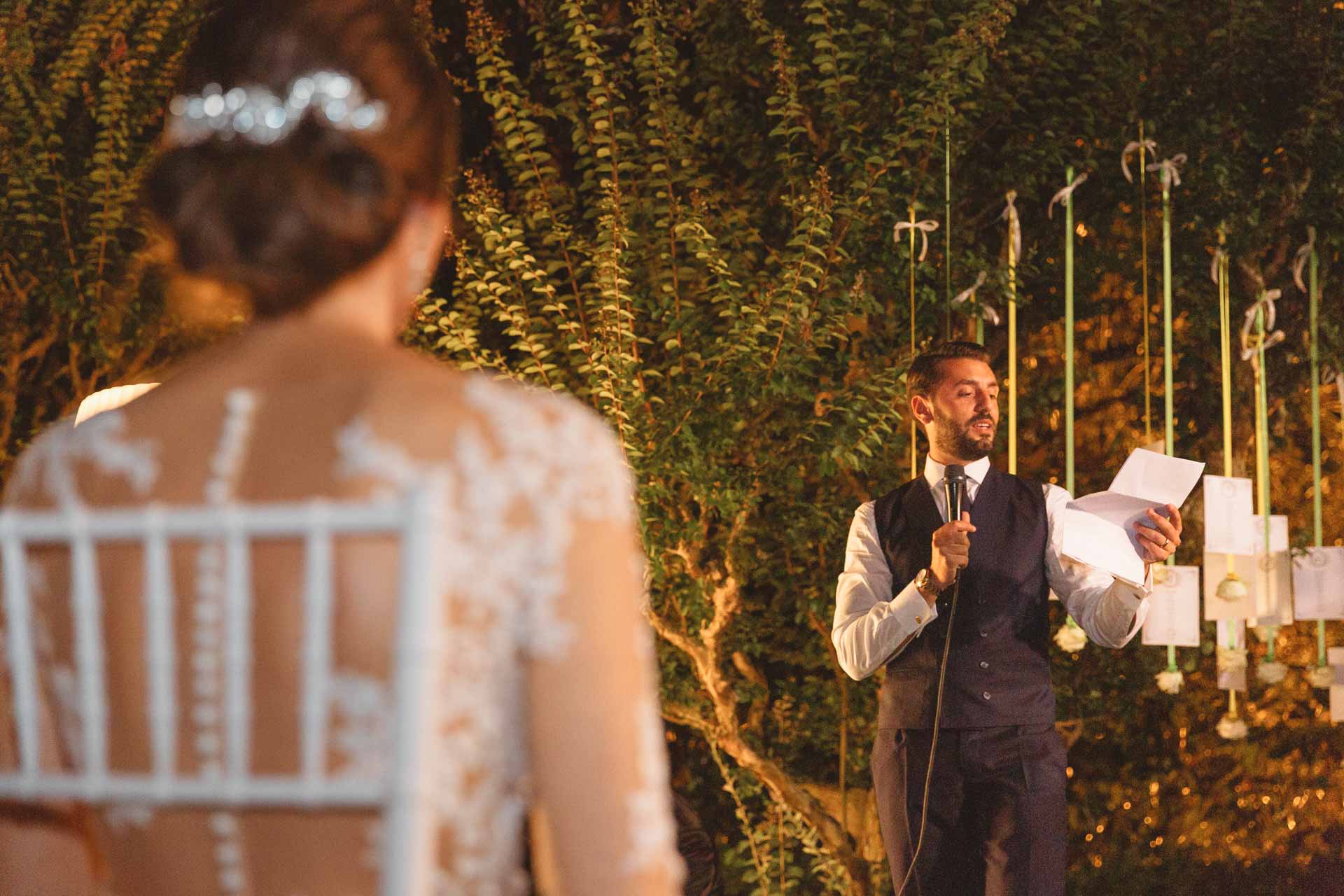 Lo sposo legge al microfono, la sposa lo guarda di spalle