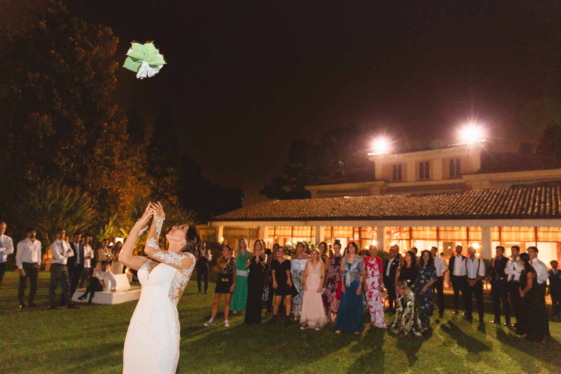La sposa lancia il bouquet davanti agli invitati e a Villa Sassi illuminata