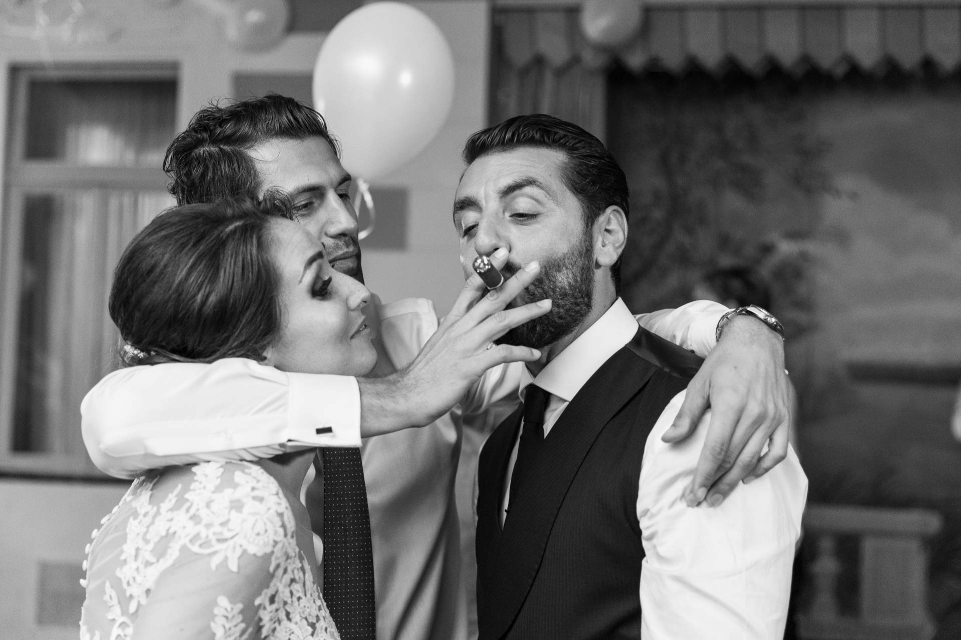 In bianco e nero, la sposa offre un sigaro allo sposo, abbracciati a un amico