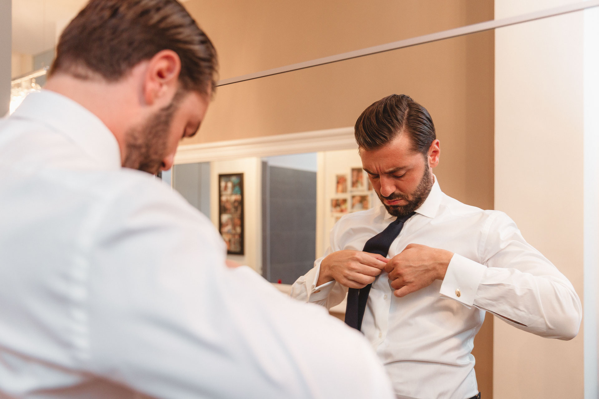 Lo sposo si annoda la cravatta allo specchio, con un amico di spalle