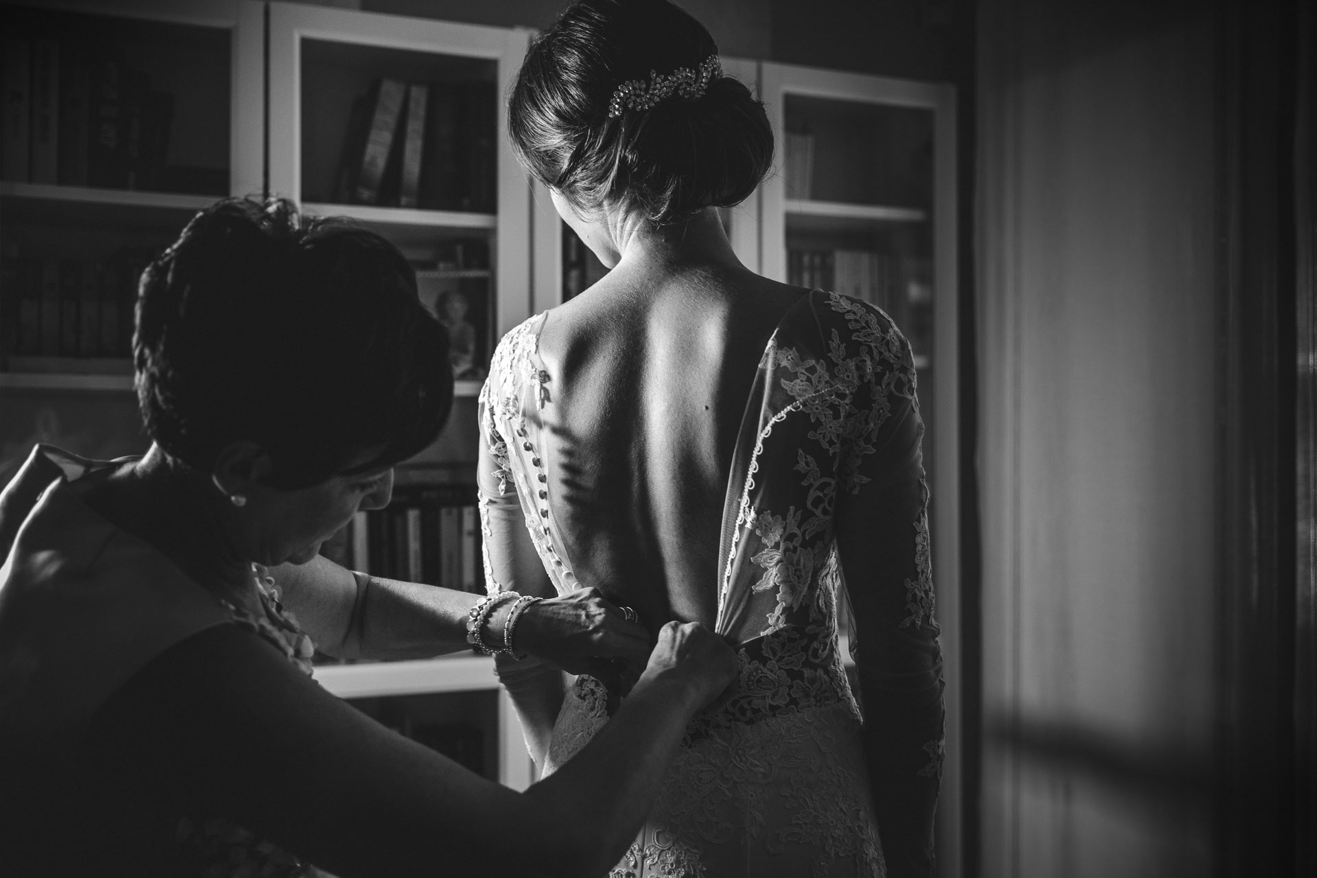 In bianco e nero, la mamma abbottona l'abito della sposa davanti alla libreria