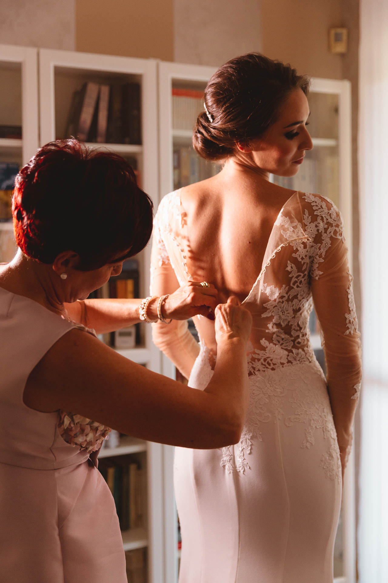 La mamma chiude l'abito di pizzo sulla schiena della sposa