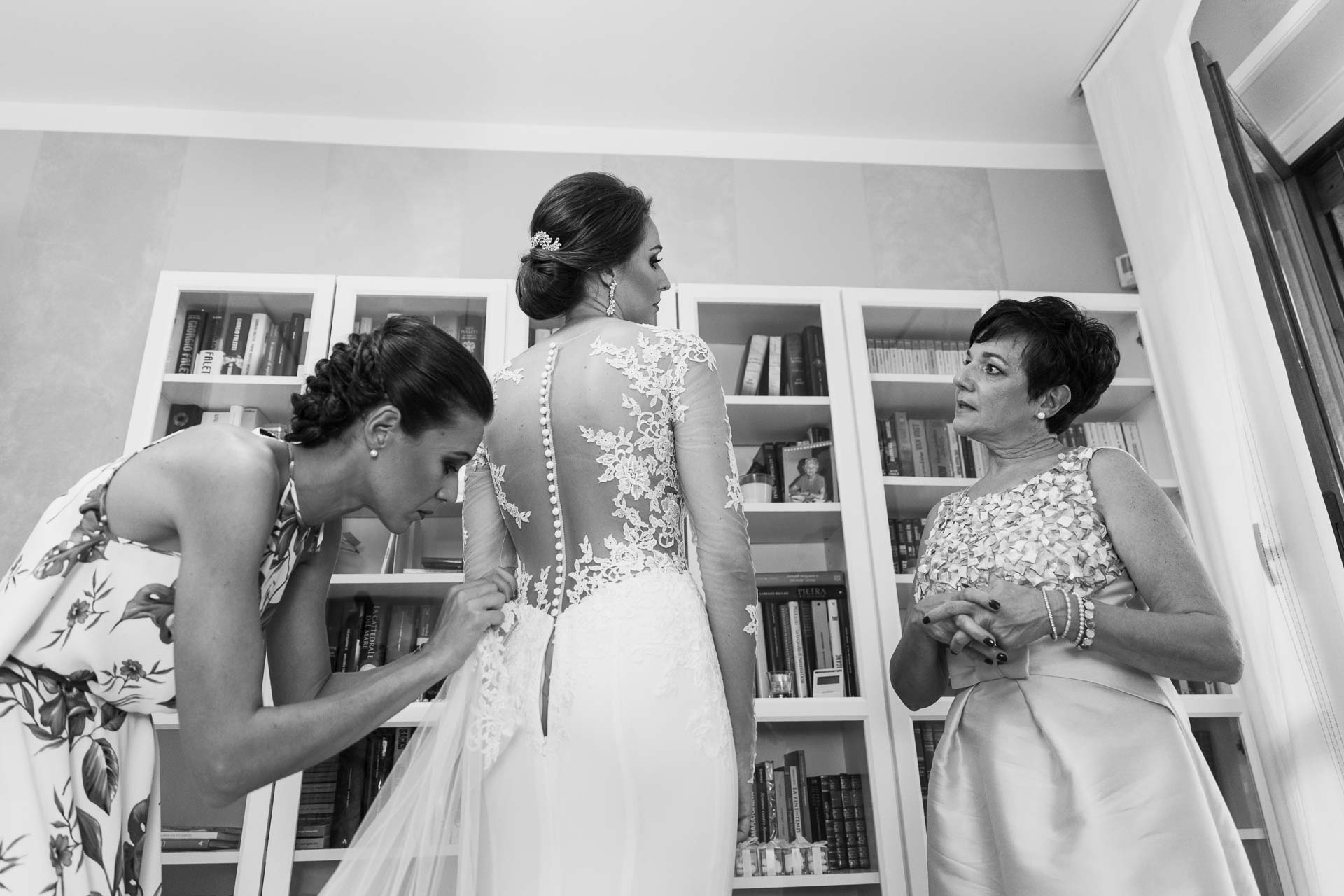 In bianco e nero, la sposa davanti alla libreria, tra l'amica e la mamma