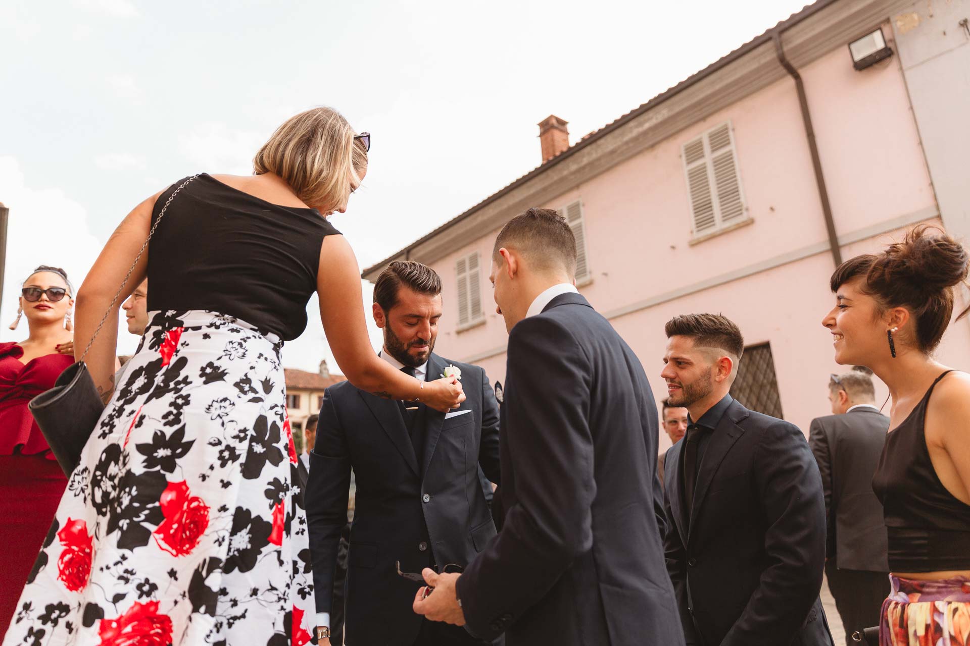 Un'invitata sistema il fiore all'occhiello allo sposo, tra gli amici